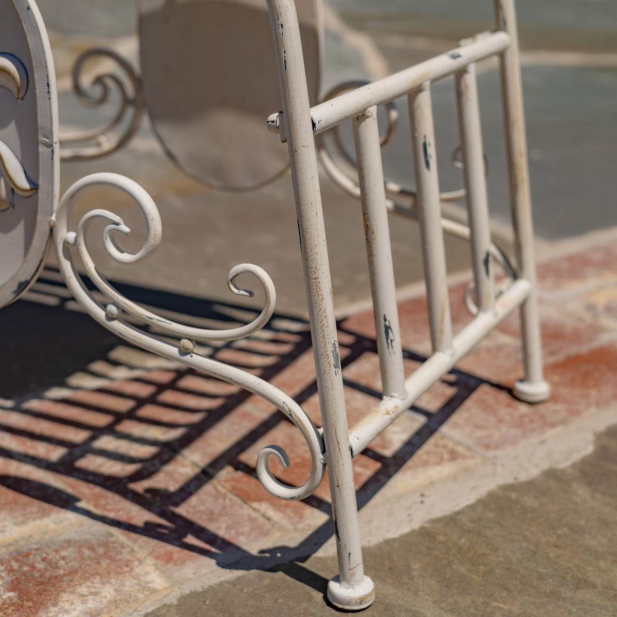 Side view of the chair’s curved metal scrollwork, slim legs, and distressed ivory finish.