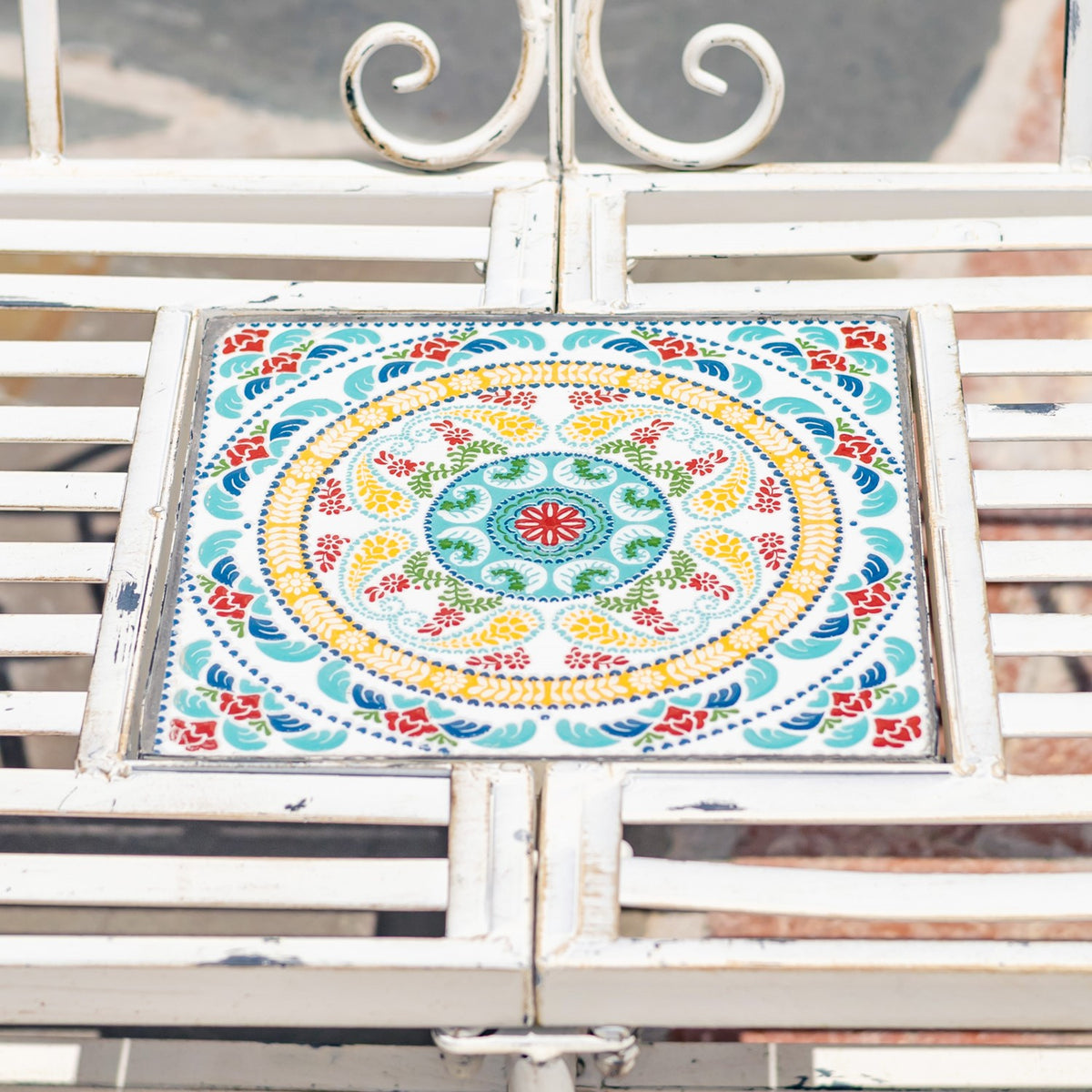 Close-up of a colorful circular floral mosaic tile inset in the white metal bench seat.