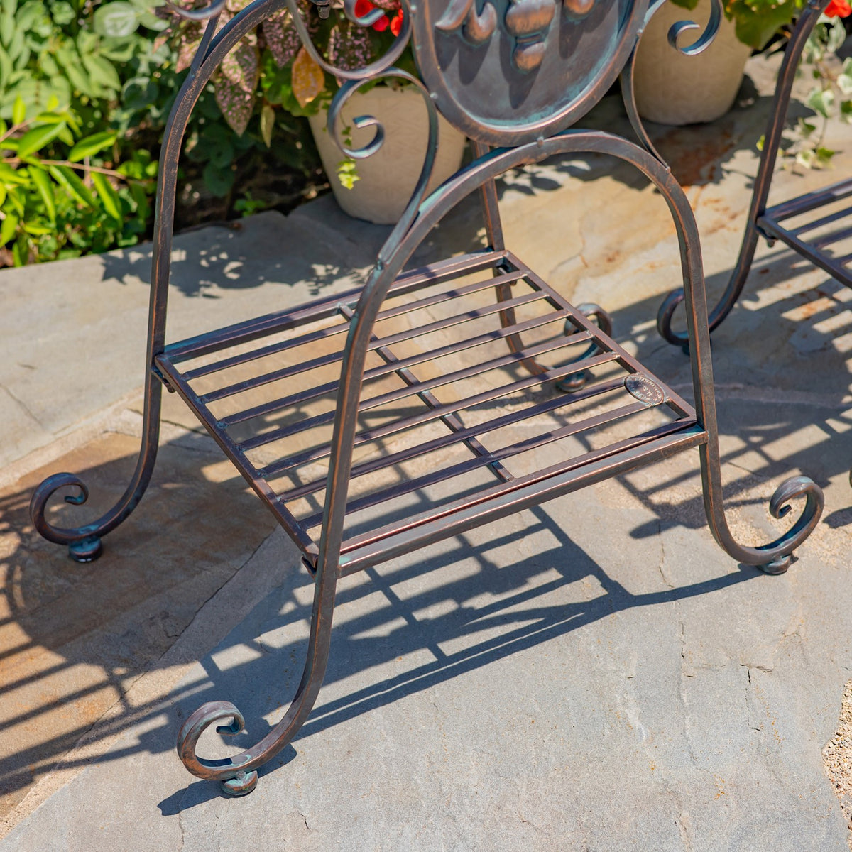 Close view of the stand’s slatted lower shelf and curved metal legs on a stone patio.