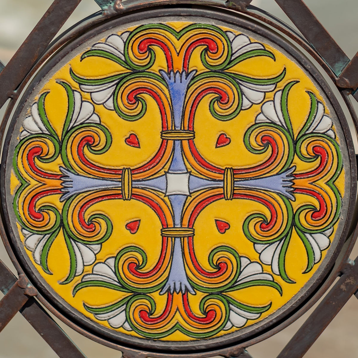 Round bench mosaic in yellow, red, green, white, and blue, framed by a dark metal rim.