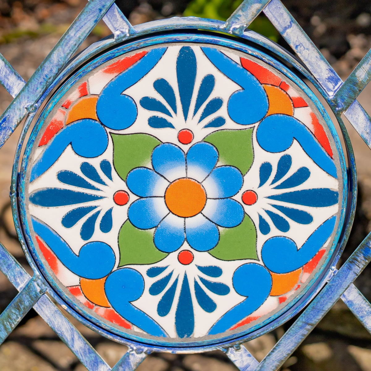 Close-up of a round mosaic tile with a blue flower and colorful geometric patterns in a metal frame.