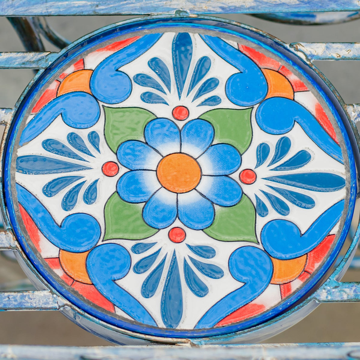Close-up of a round mosaic surface with a blue, white, green, and orange floral pattern.