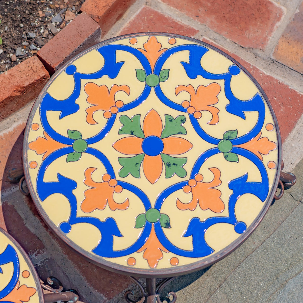 A round mosaic plant stand viewed from above, showing a blue, orange, green, and cream floral pattern.