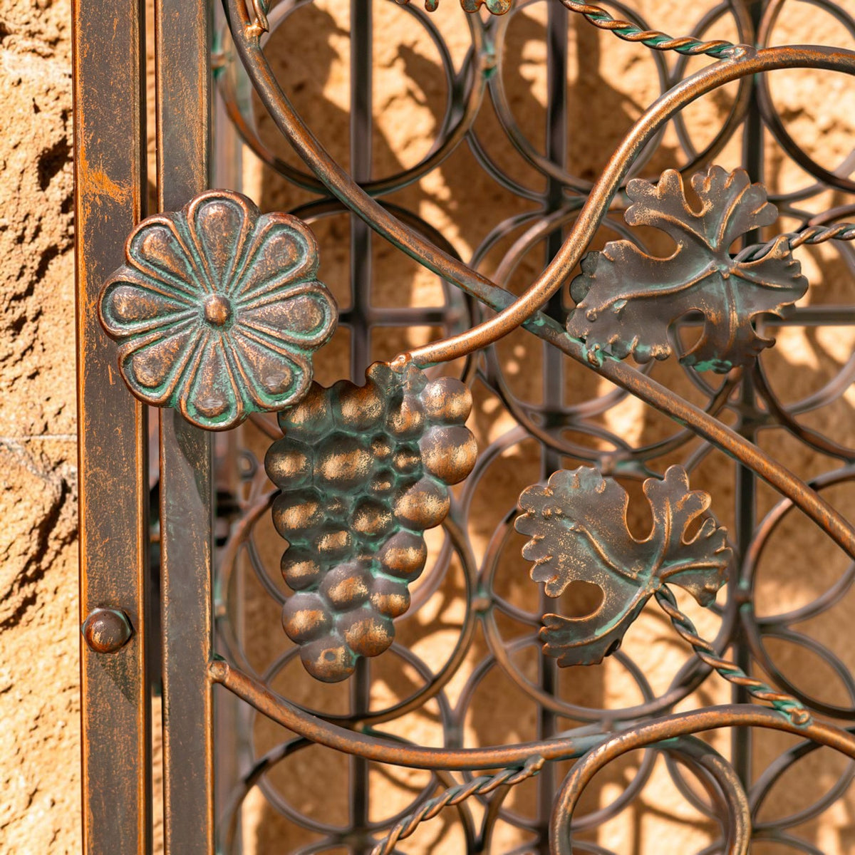 Close-up of raised grape and flower ornaments on the rack’s bronze-toned iron scrollwork.