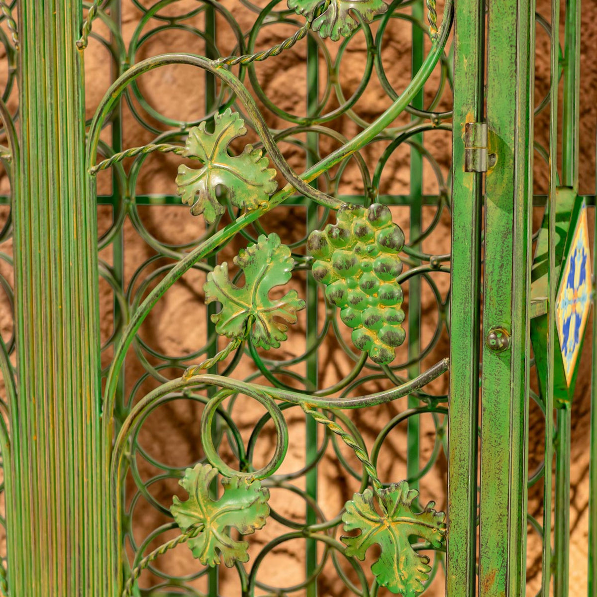 Green iron scrollwork with grape and leaf motifs beside a small cabinet hinge.