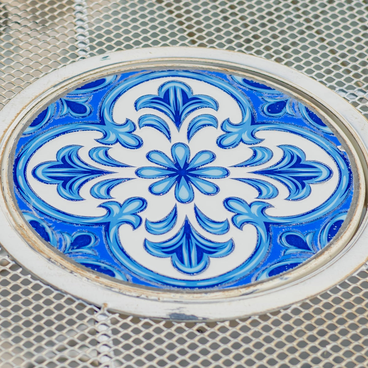 Blue-and-white floral mosaic medallion set into the center of a pale metal mesh tabletop.