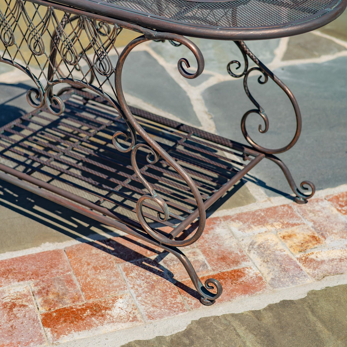 Close side view of the table’s curled metal legs and open lattice shelf on a stone patio.