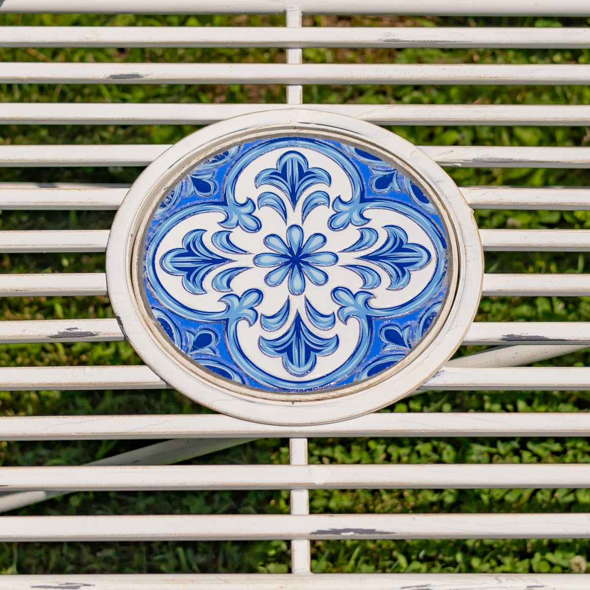 Close-up of a blue floral medallion set among the bench’s white metal seat slats.