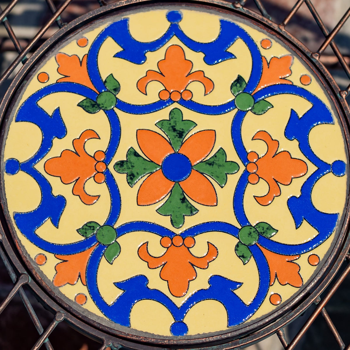 Round bench mosaic with a vivid blue, orange, green, and cream floral pattern set in a dark metal frame.