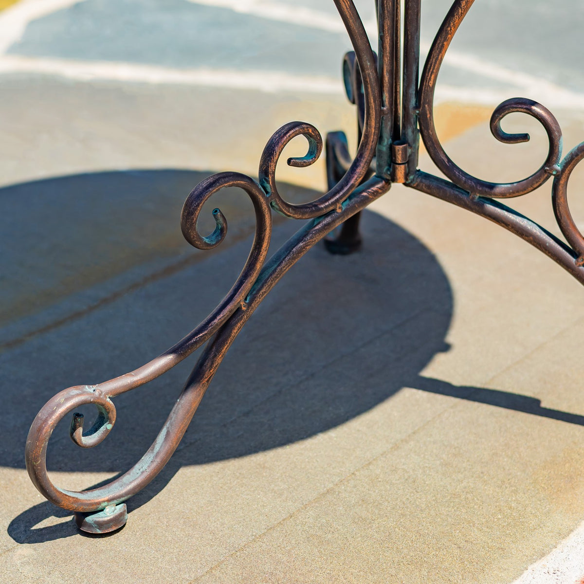 Close view of the stand’s scrollwork legs, showing textured dark metal and rounded feet.