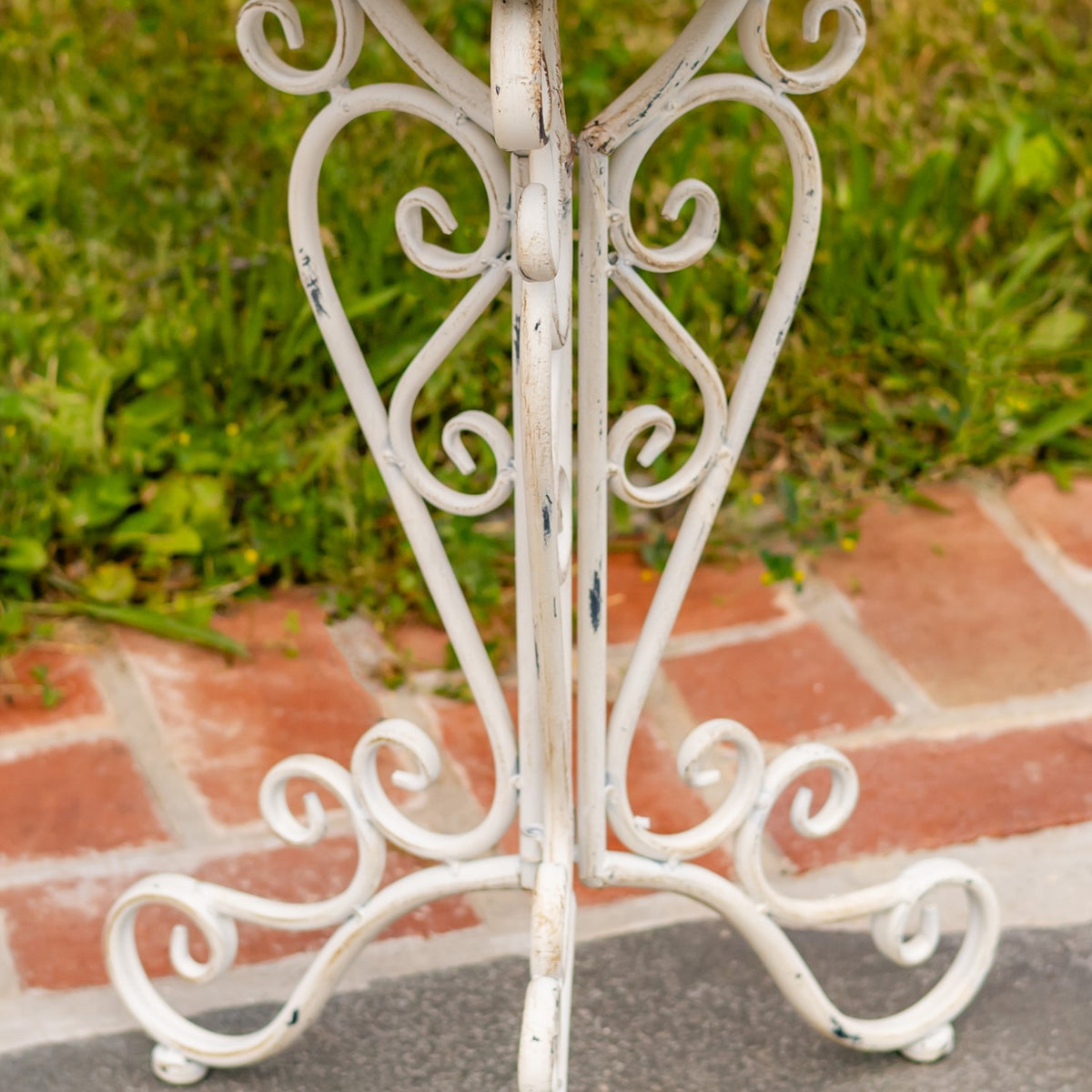 Close-up of the stand’s curved white metal legs and scrolling feet on a brick path.