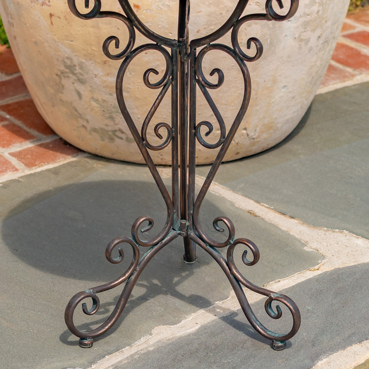 Close view of the dark metal stand’s curled scrollwork legs and central support.