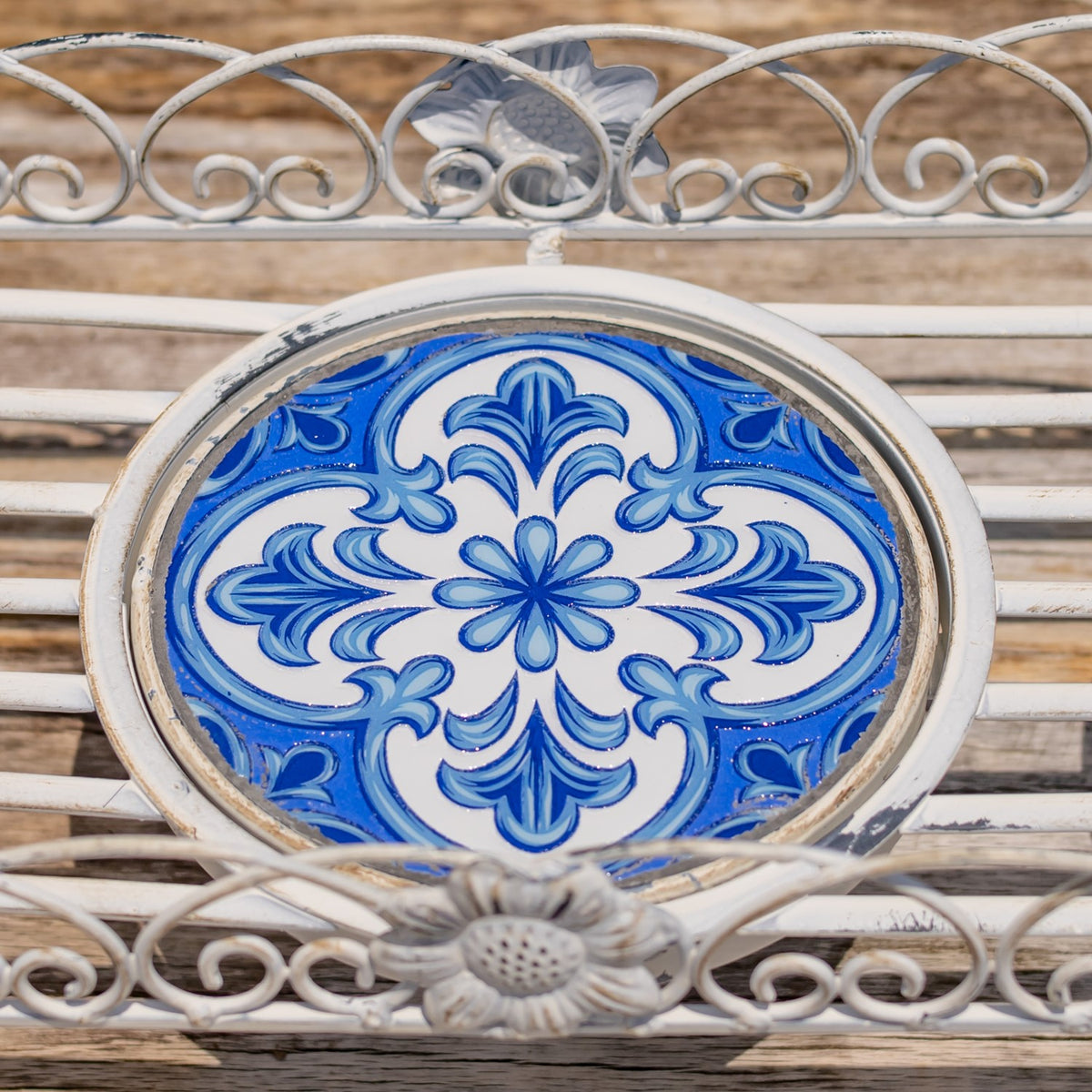Close-up of a blue-and-white floral mosaic tile framed by ornate pale metal scrollwork.