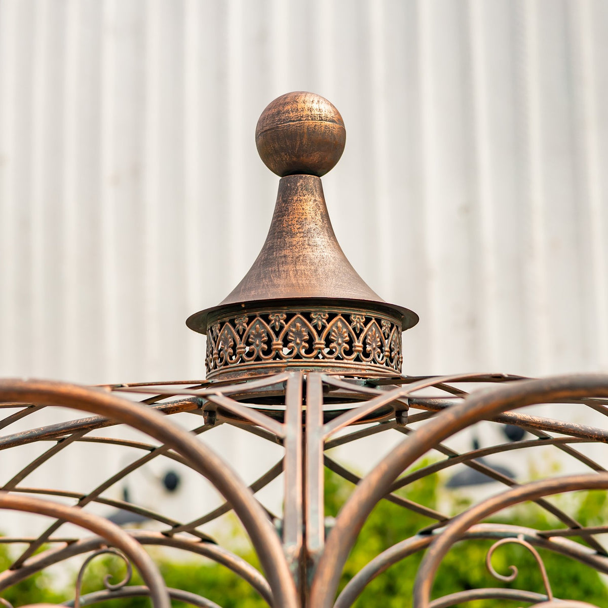 A bronze-toned ball finial and flared cap rise above the bridge’s curved metal framework.