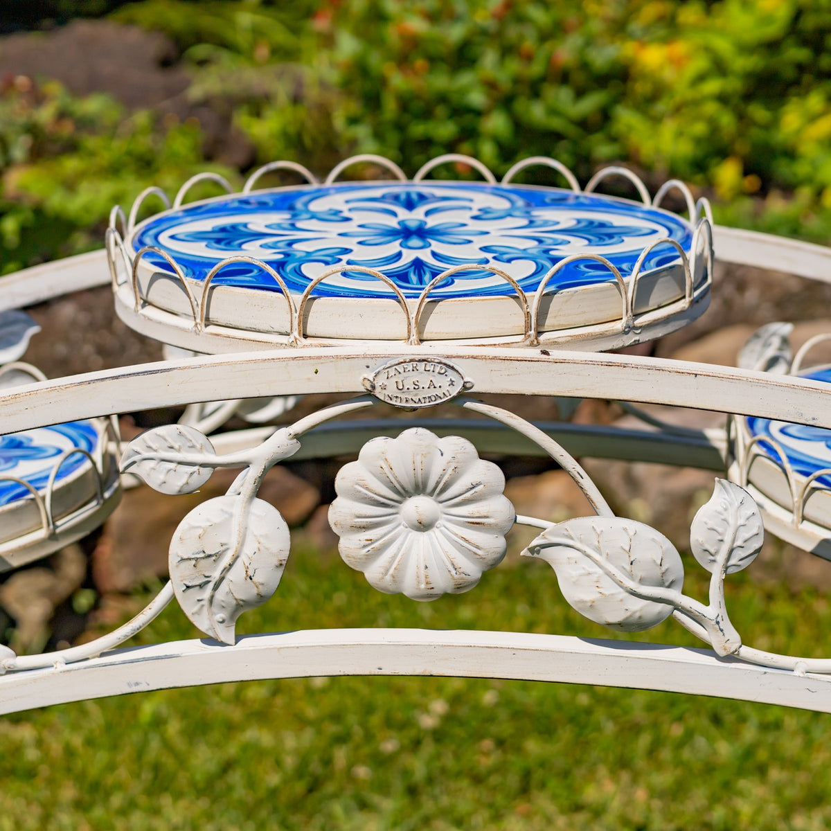 Close-up of a blue-and-white mosaic platform above white metal flower and leaf decorations.