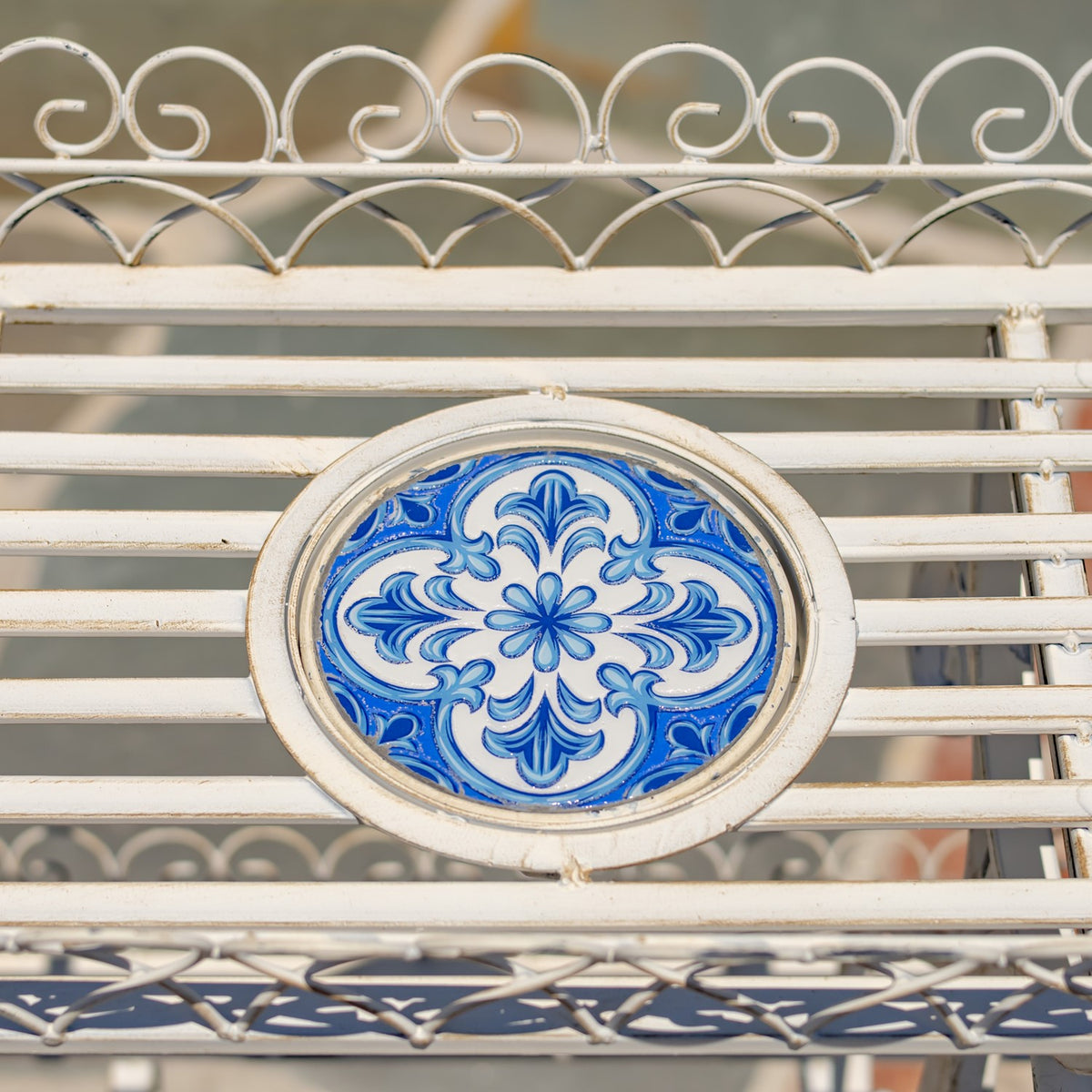 Close-up of a blue floral mosaic medallion set into the stand’s white iron slats and curled railing.