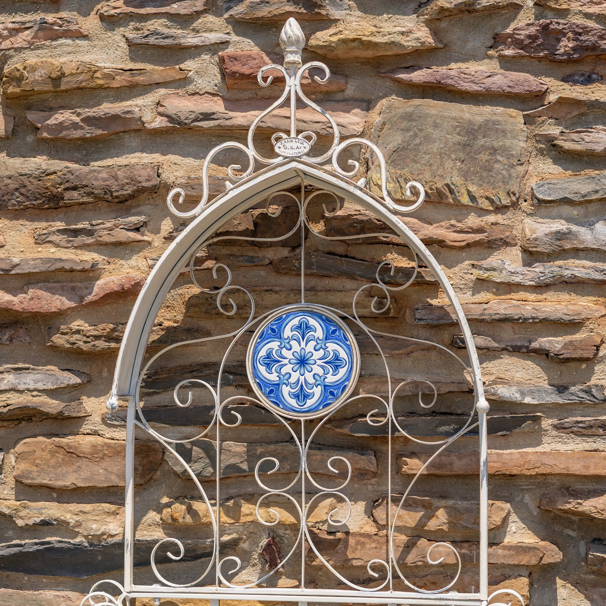 Ornate white metal wall planter with curling scrollwork and a blue-and-white mosaic medallion.