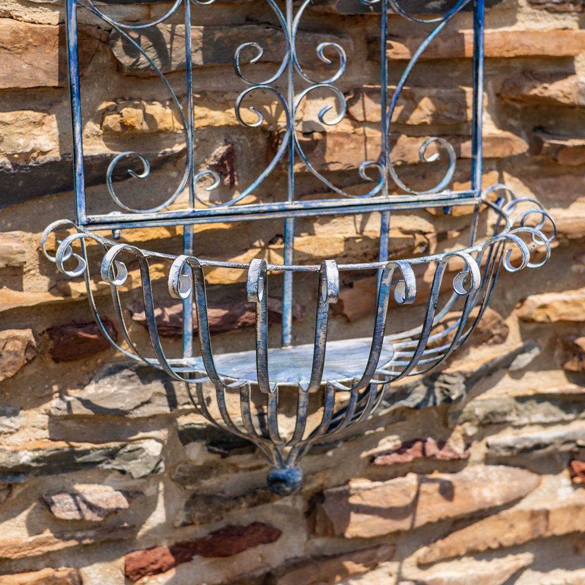 Close-up of the curved iron basket and hanging hooks beneath the planter’s scrollwork.