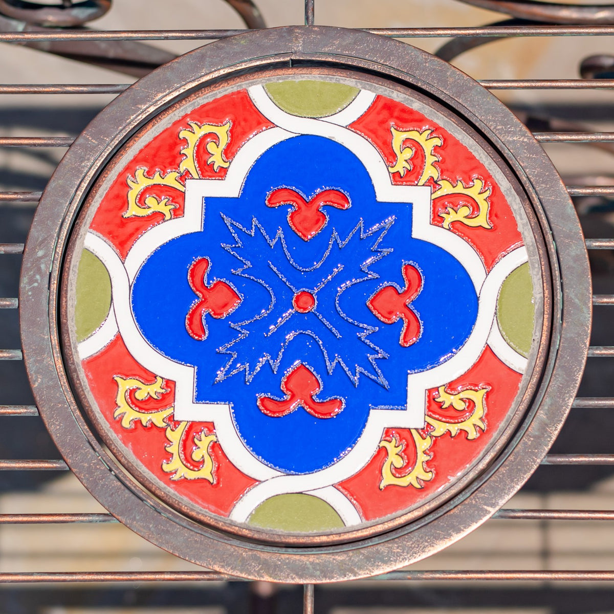Round tabletop mosaic with a vivid blue center, red and cream shapes, and a bronze-toned rim.