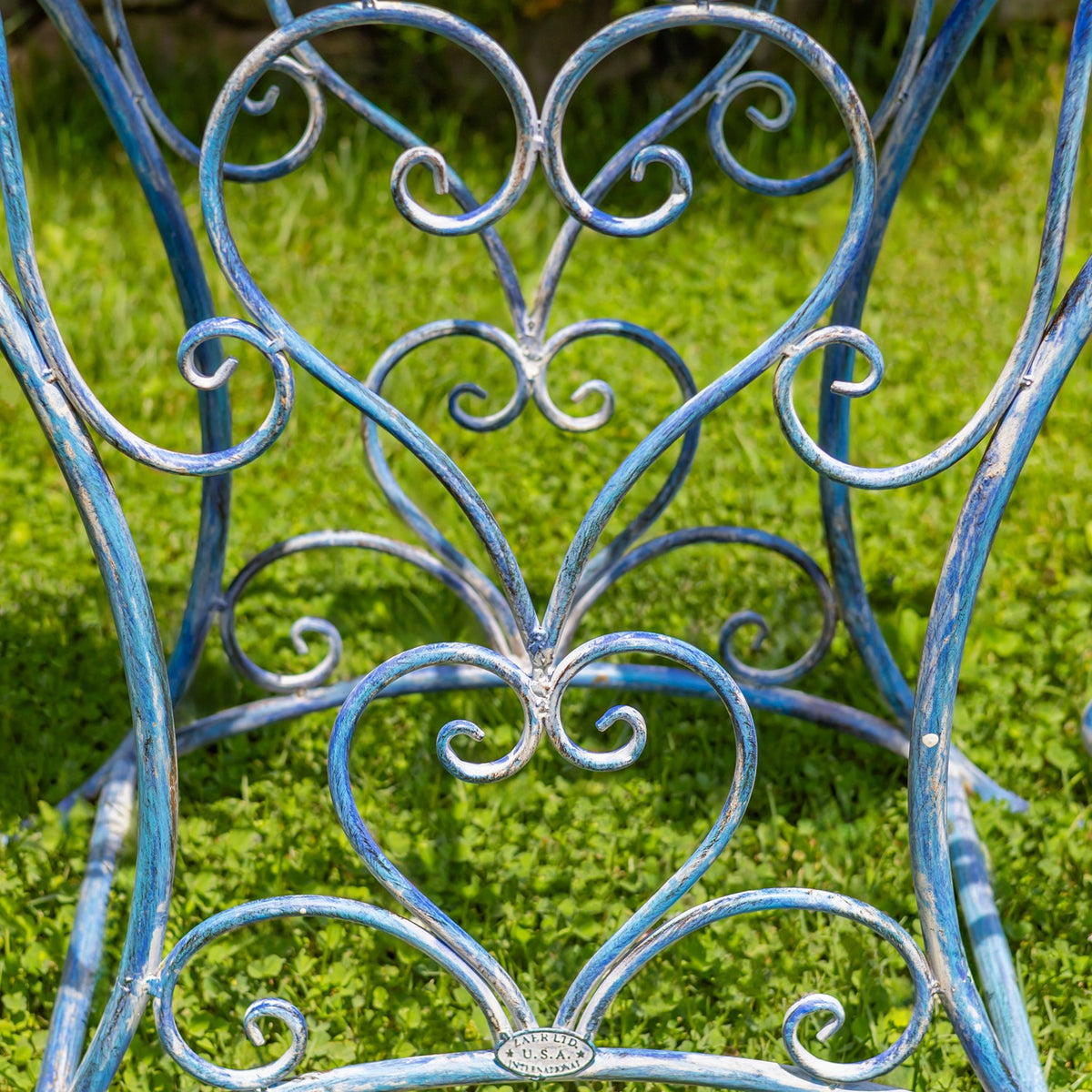 Close-up of curved blue iron legs with decorative heart-shaped scrollwork against a grassy background.
