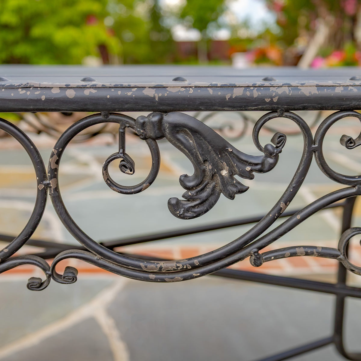 Close view of curled metal ornament and chipped finish along the edge of an outdoor table.