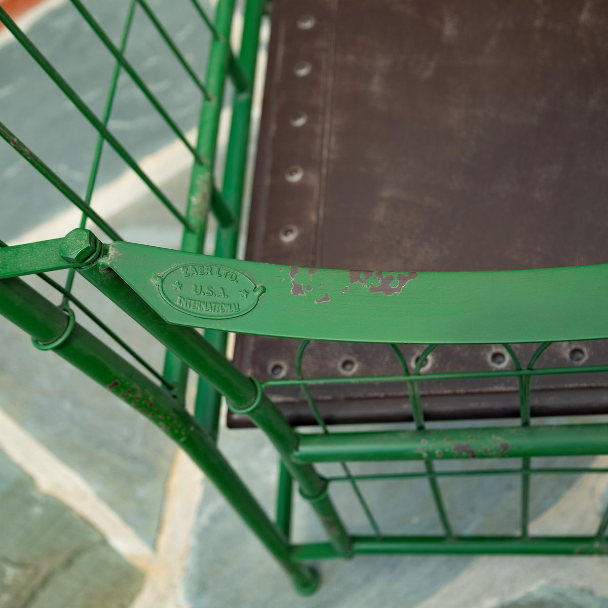 Close-up of a green metal armrest with chipped paint beside the chair’s brown seat