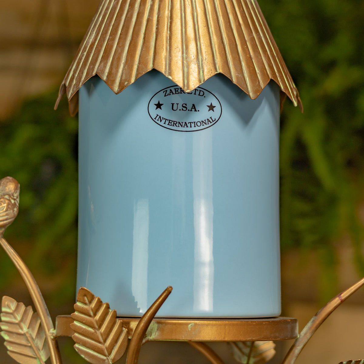 Close view of the glossy blue birdhouse body, scalloped metal roof edge, and decorative leaf base.