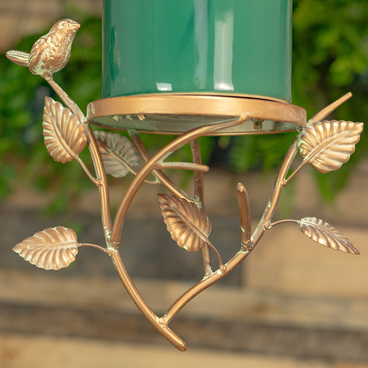 Close view of the birdhouse’s gold-toned metal branches, leaves, and small perched bird beneath the green body.