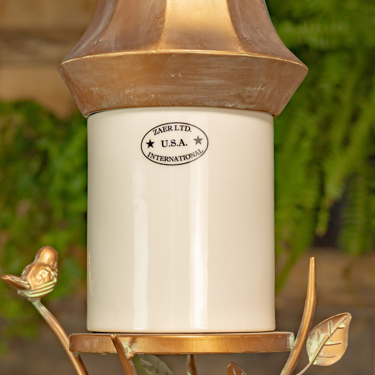 Close view of the white cylindrical body beneath a flared bronze-tone roof, with a bird ornament and leaves nearby.