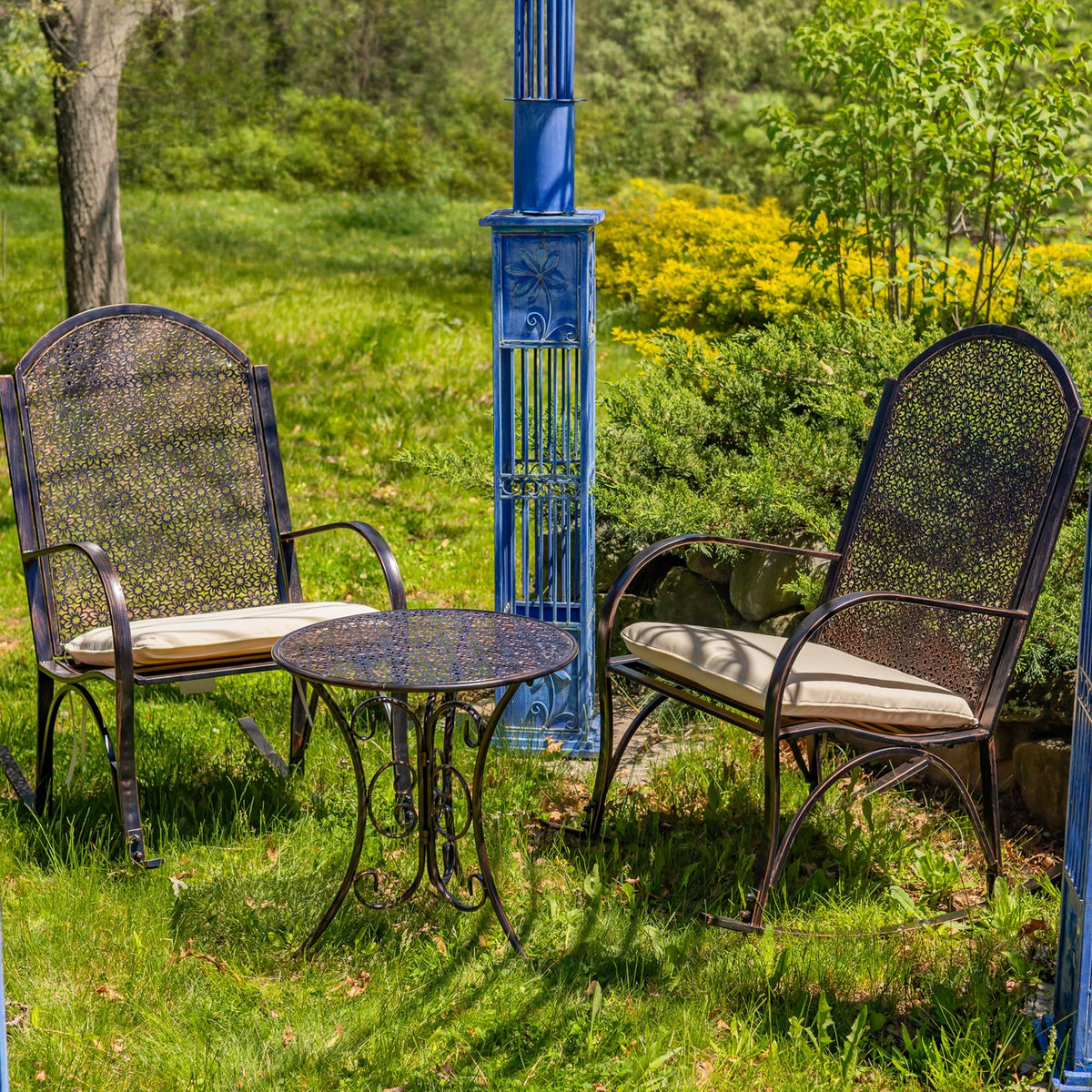 Two metal rocking chairs with light cushions flank a small round table in a garden.