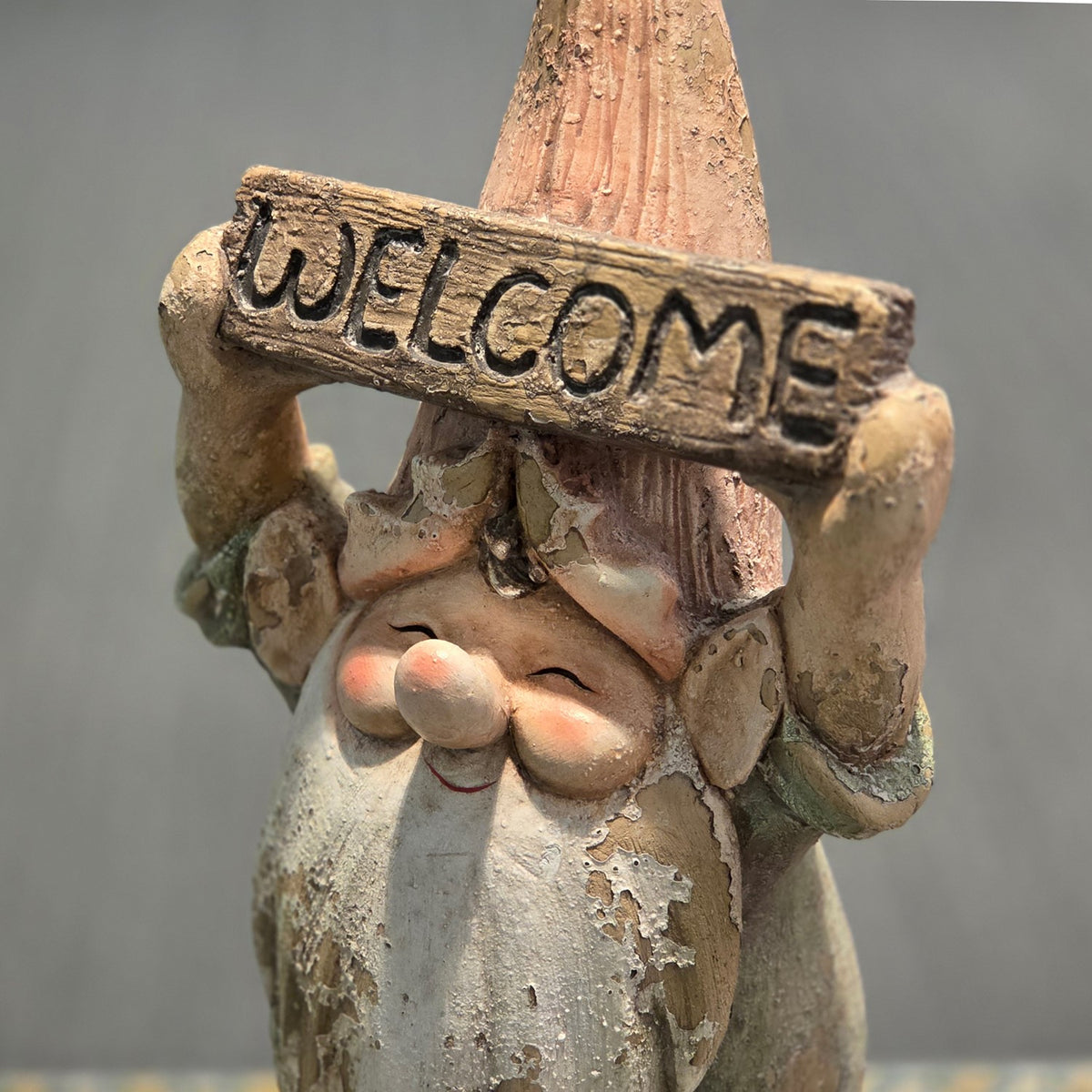 Close front view of a smiling garden gnome holding a welcome sign overhead