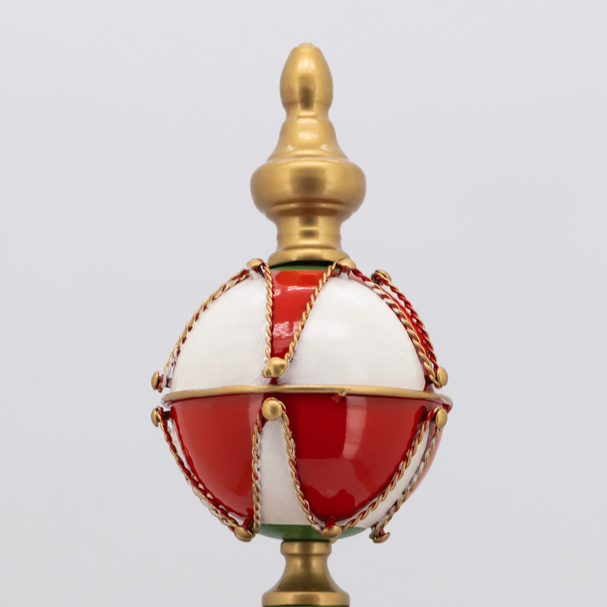 Close-up of a glossy red-and-white ornament with braided gold trim and a sculpted gold finial.