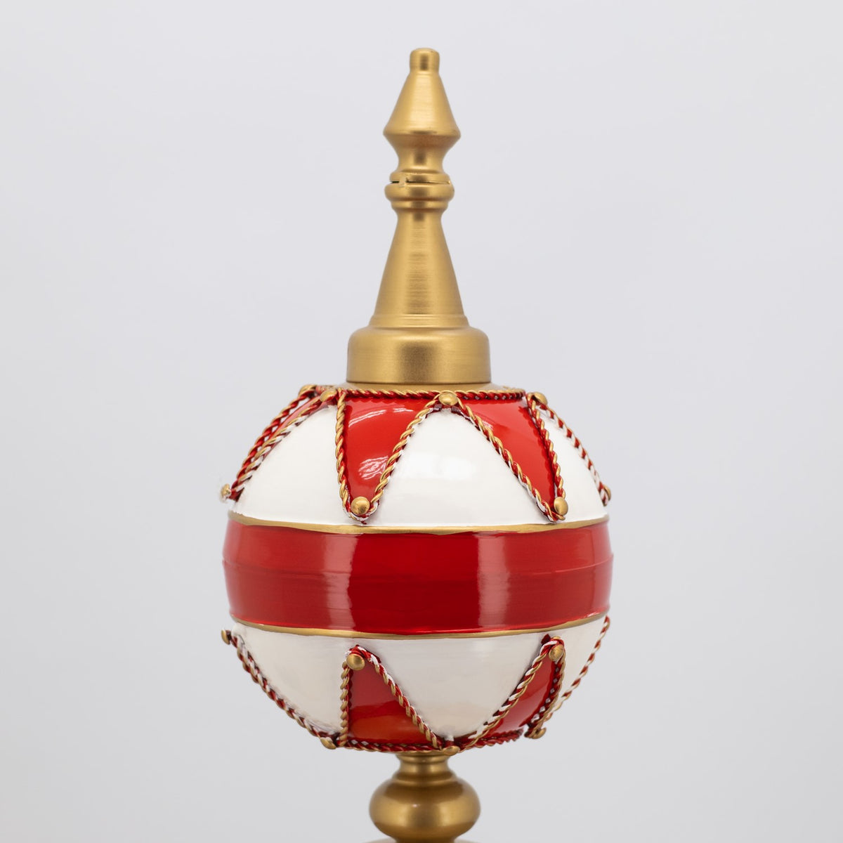 Close view of the upper red and white ornament with gold trim and a pointed finial.