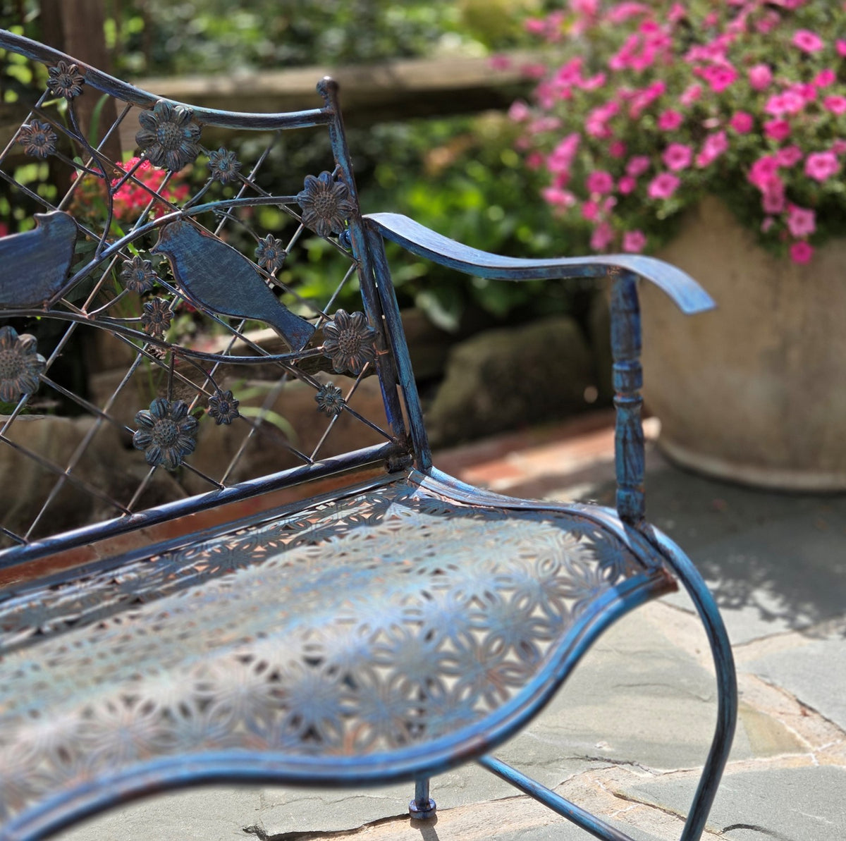 Angled view of the garden bench showing its floral bird backrest, patterned seat, and curved armrest.