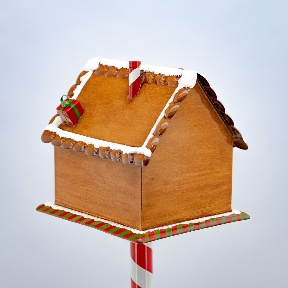 Wood-toned gingerbread mailbox with a snowy roof, gift decoration, and striped candy cane post.