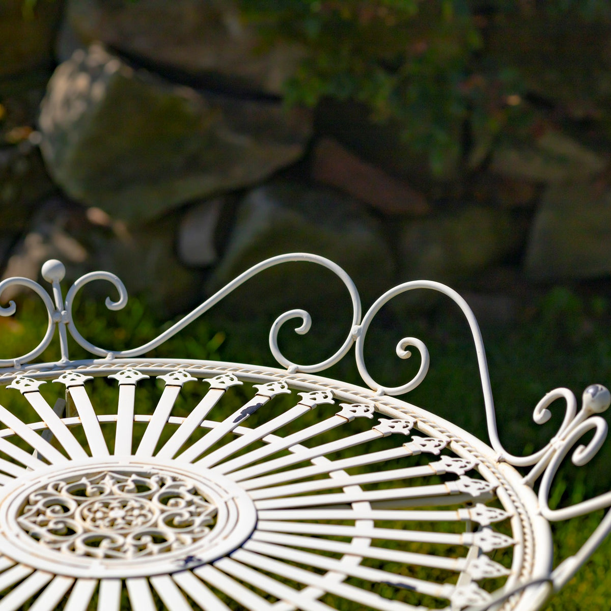 Close-up of an ornate white metal garden table top with scrolling edge details against a stone backdrop.