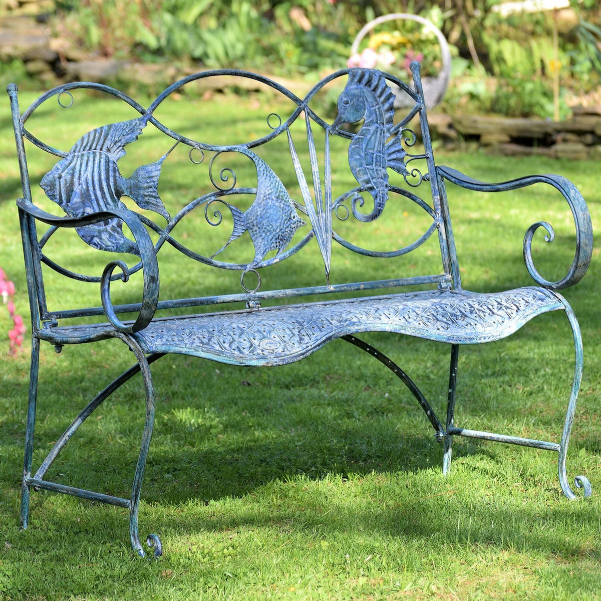 Coastal blue metal garden bench with curled arms and two seahorse decorations on the back, set on grass.