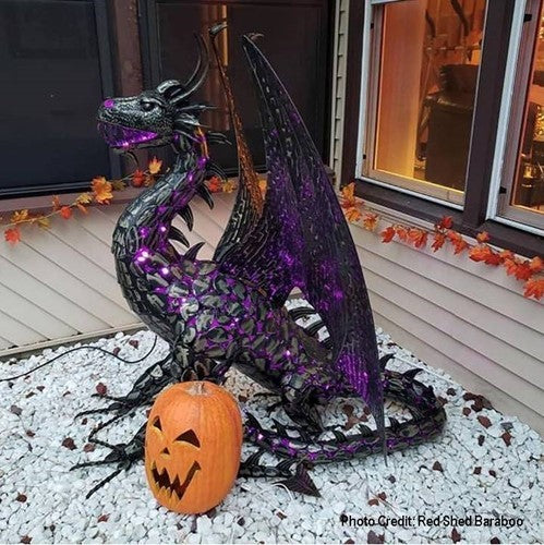 A dragon statue glows with purple lights beside a carved pumpkin on a bed of white stones.