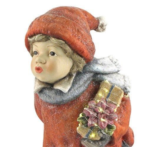 Close-up of a child figurine in a red winter hat holding a small bundle of gifts.