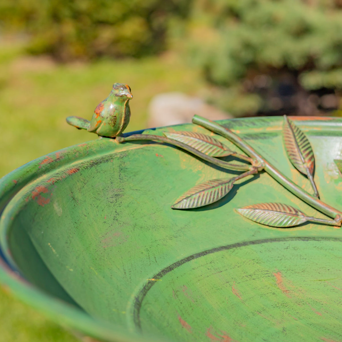 Close view of a small bird ornament and textured green surface with raised metal leaves.