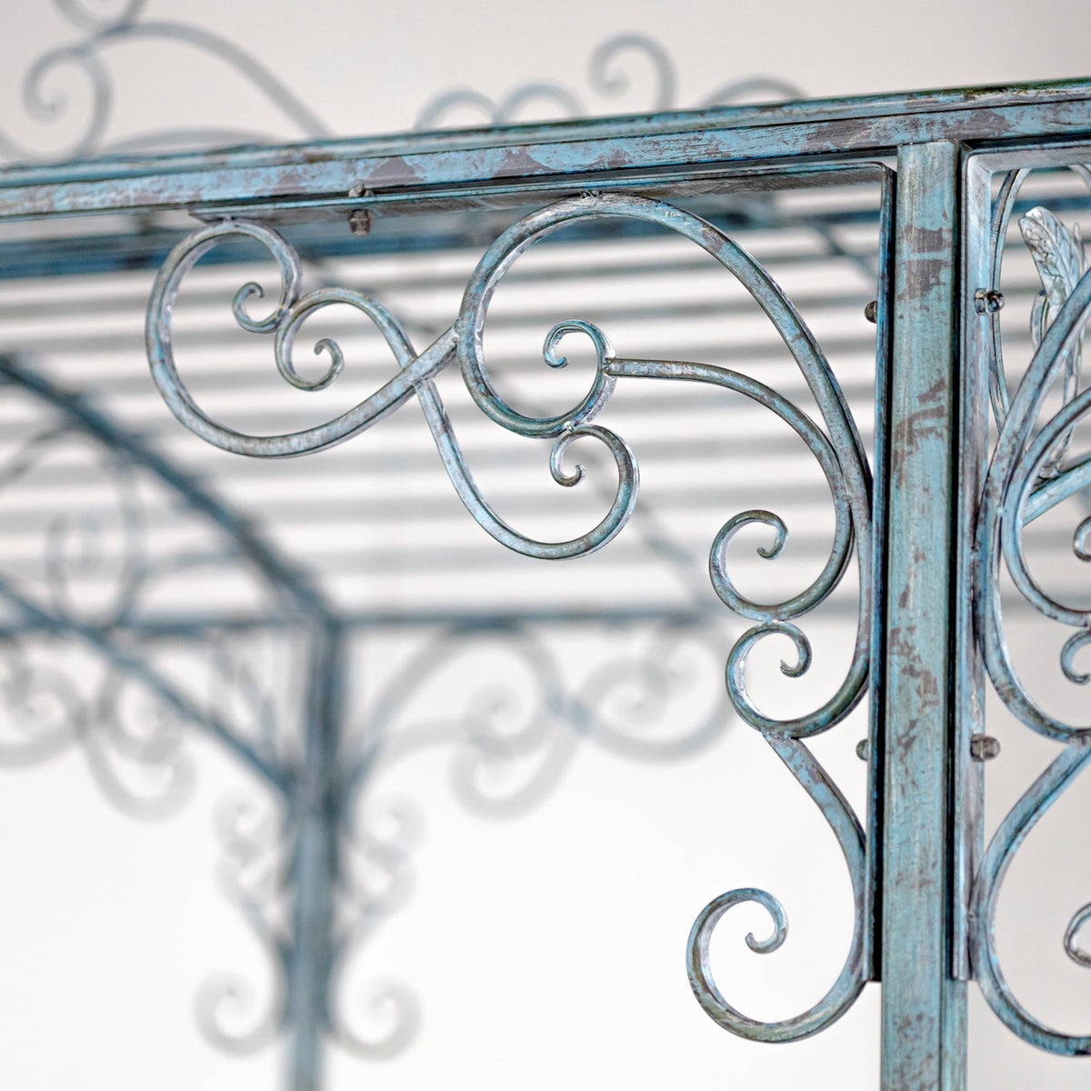Curled blue-gray iron scrollwork framed by a square post, with the gazebo structure blurred behind it.