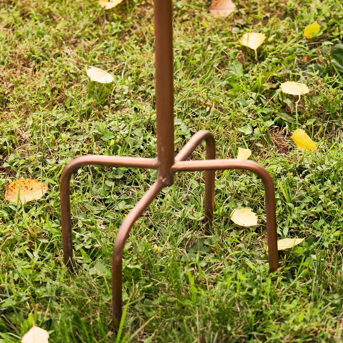 Close-up of the brown metal stake ending in curved legs pressed into grass.