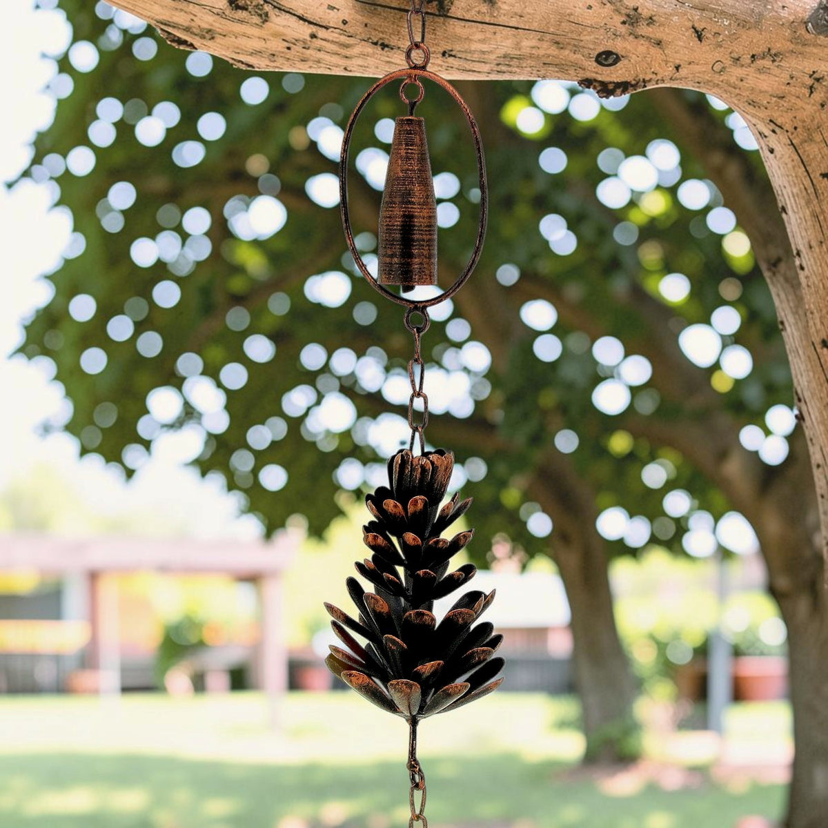 A pinecone pendant and oval-framed cylinder hang together as part of a rain chain.