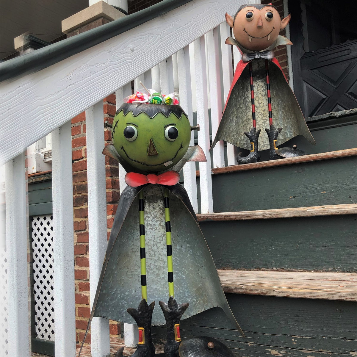 Green monster candy jar stands on porch steps beside a vampire figurine.