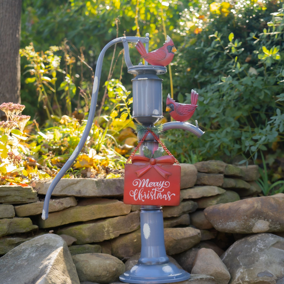 The blue pump decoration stands against a low stone wall, with cardinals and a red sign among sunlit greenery.