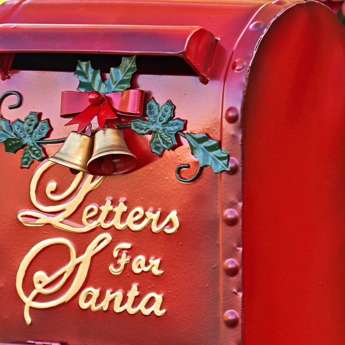 Close-up of a red mailbox decorated with holly, bells, a bow, and raised gold lettering.