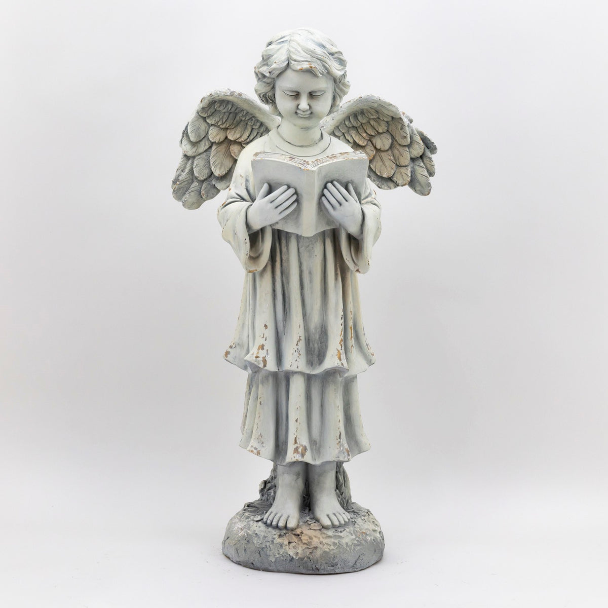 Full front view of a winged angel statue standing barefoot and reading an open book.