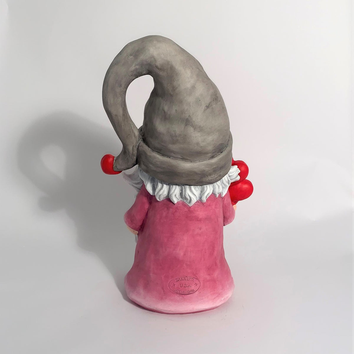 Rear view of the gnome in a gray floppy hat and pink outfit, with part of its red balloons visible.