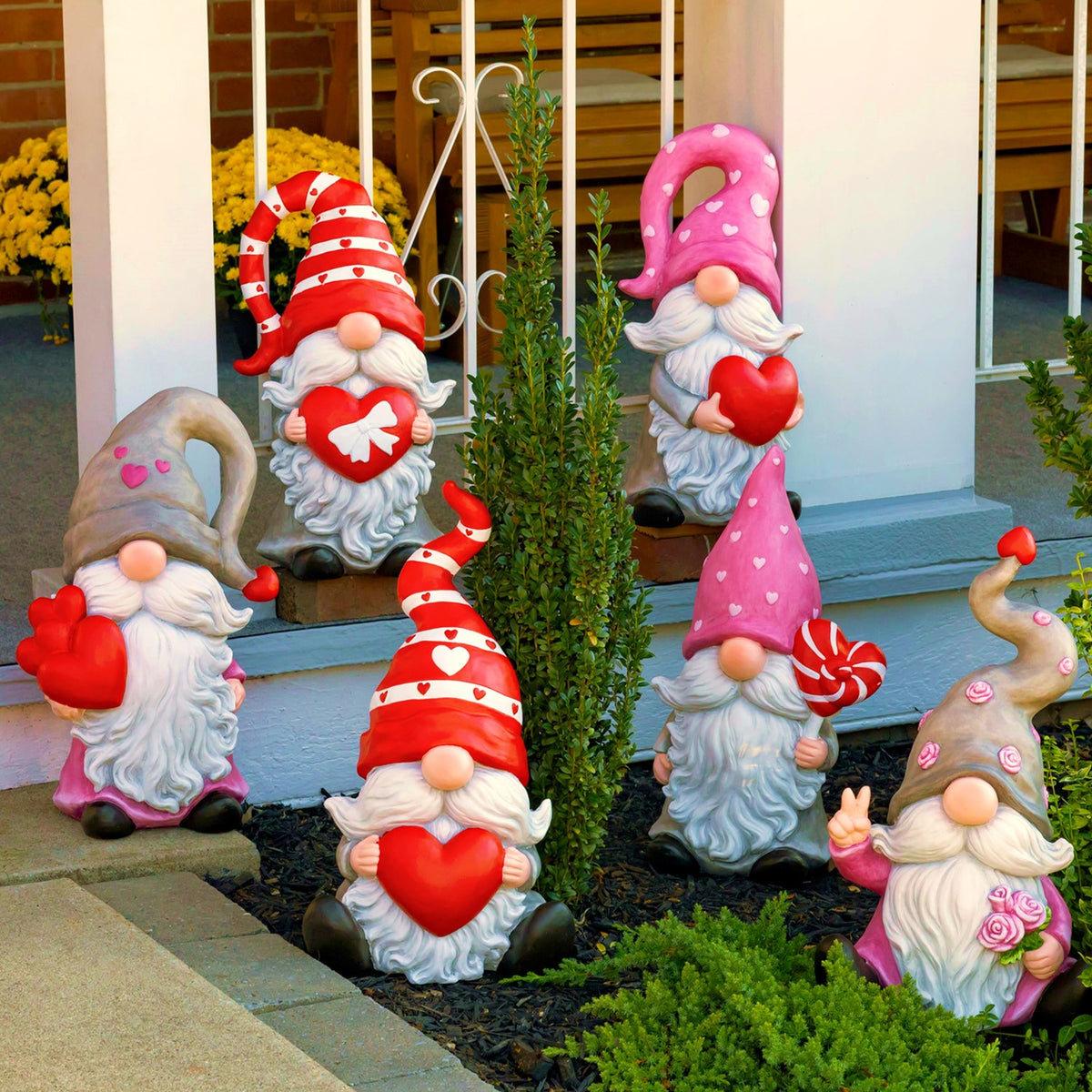 Six colorful Valentine gnome figures arranged among plants beside a porch