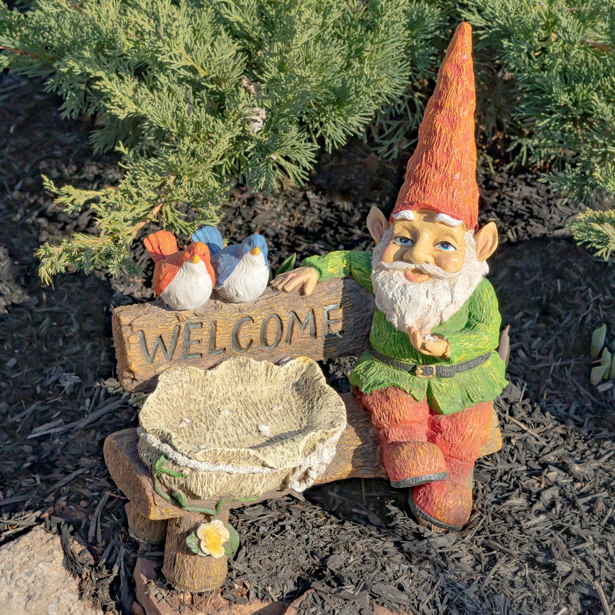 Garden gnome seated beside a birdbath and welcome sign, with two small birds perched on the sign.